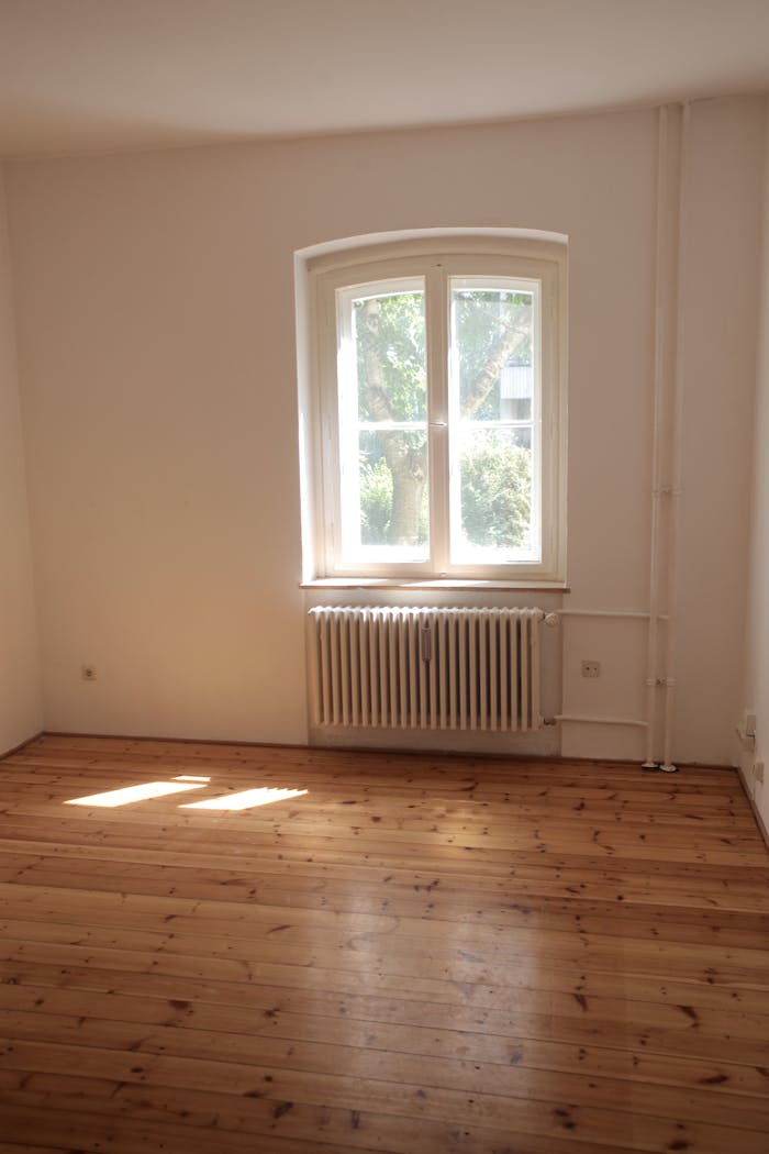 Services Spacious empty room with wooden floor and large window in Berlin, ideal for interior planning.